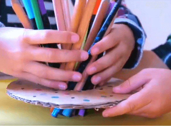 Kid hands holding pens and pencils, cardboard in shape of a donut.