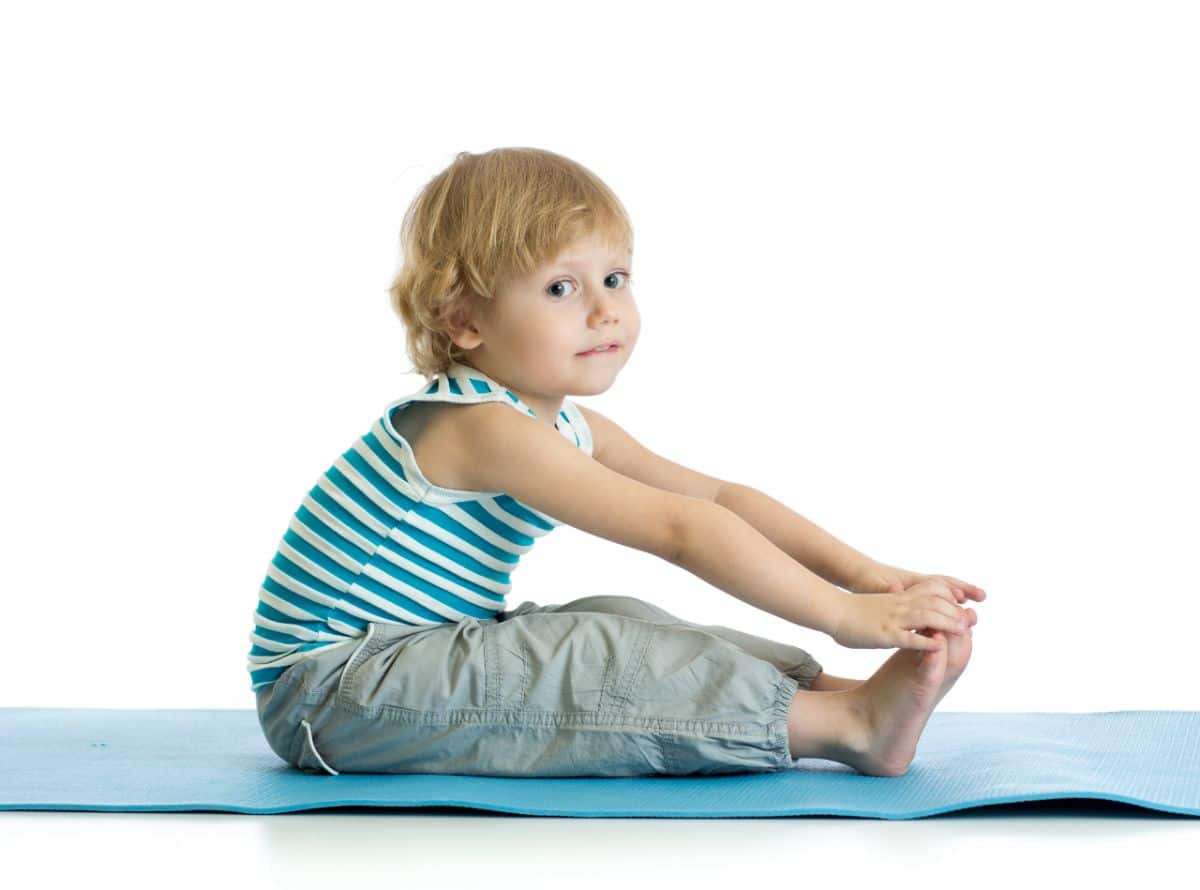 Young boy sitting a nd stretching on a yoga pad.