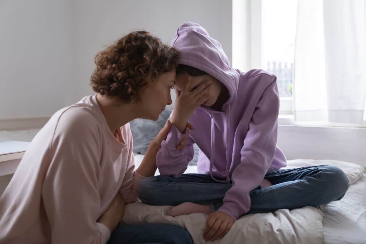 Mother comforting a depressed daughter on a bed.