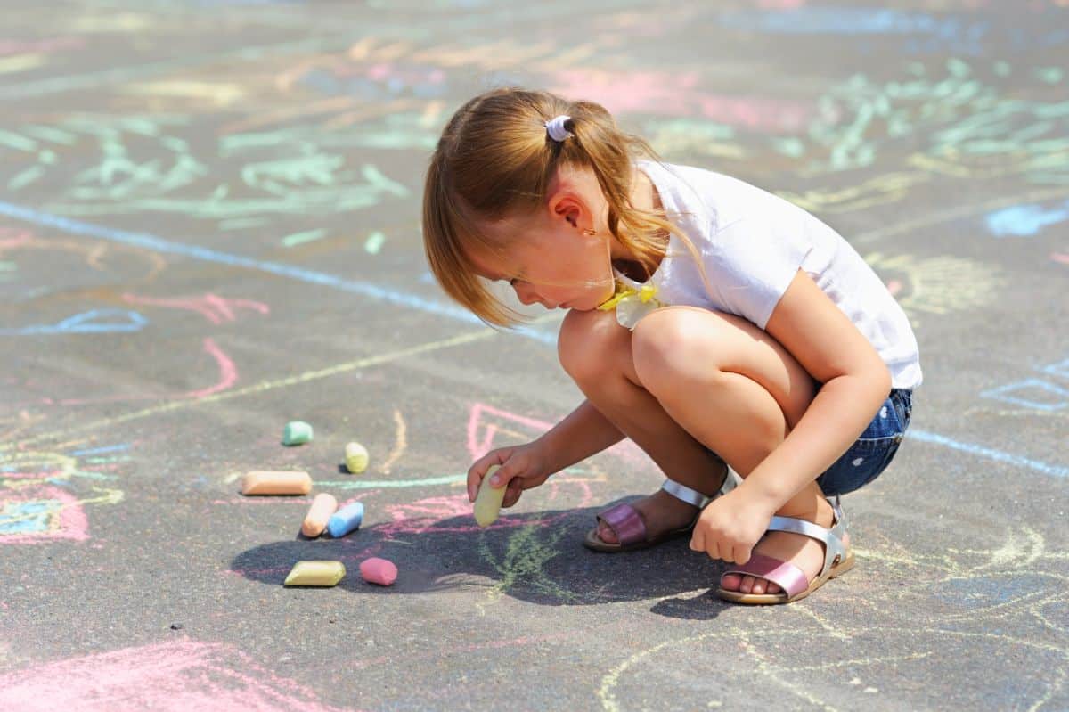 Little girl drawing with chalks on a sidewalk.