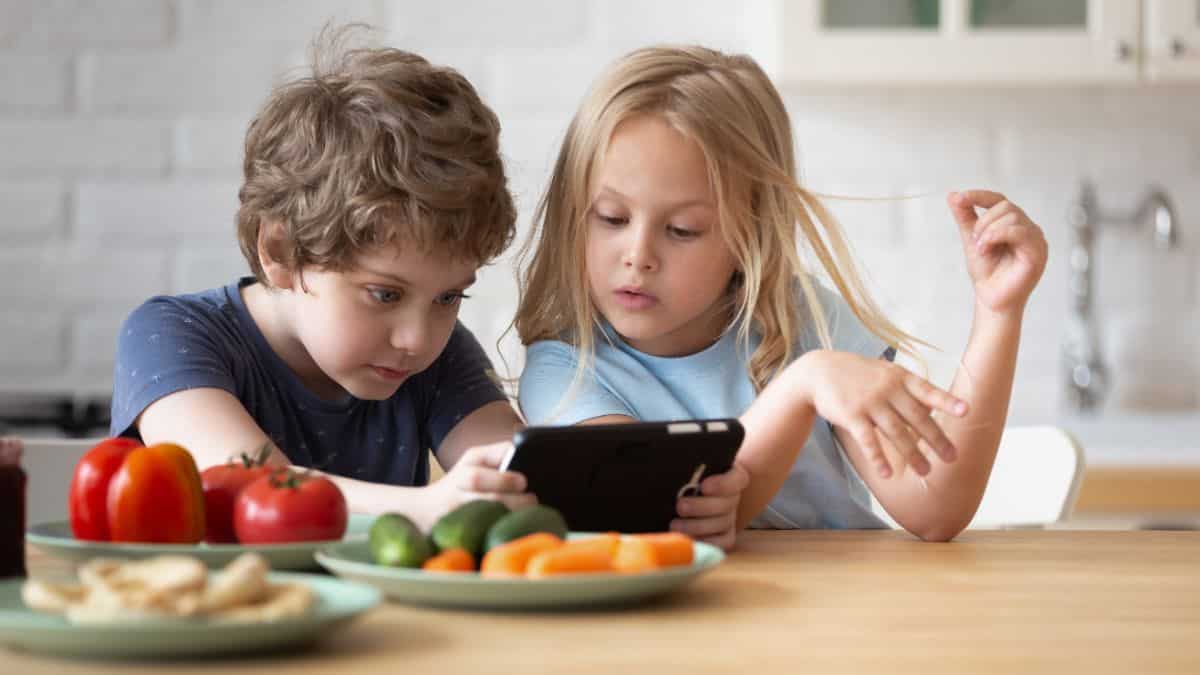 Two young kids sitting behind the desk and looking  at tablet.