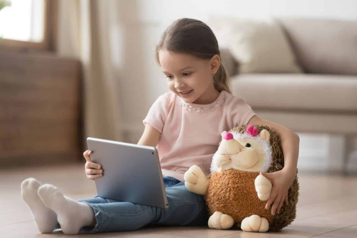 Young girl holding a stuffed toy and looking at  tablet.