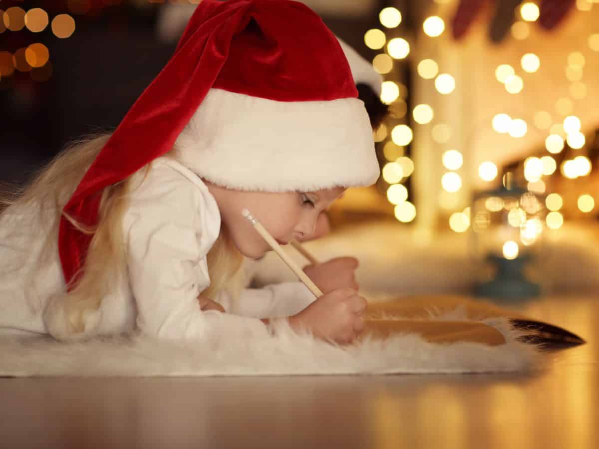 Young girl with christmas hat lying on the floor and writing a letter.