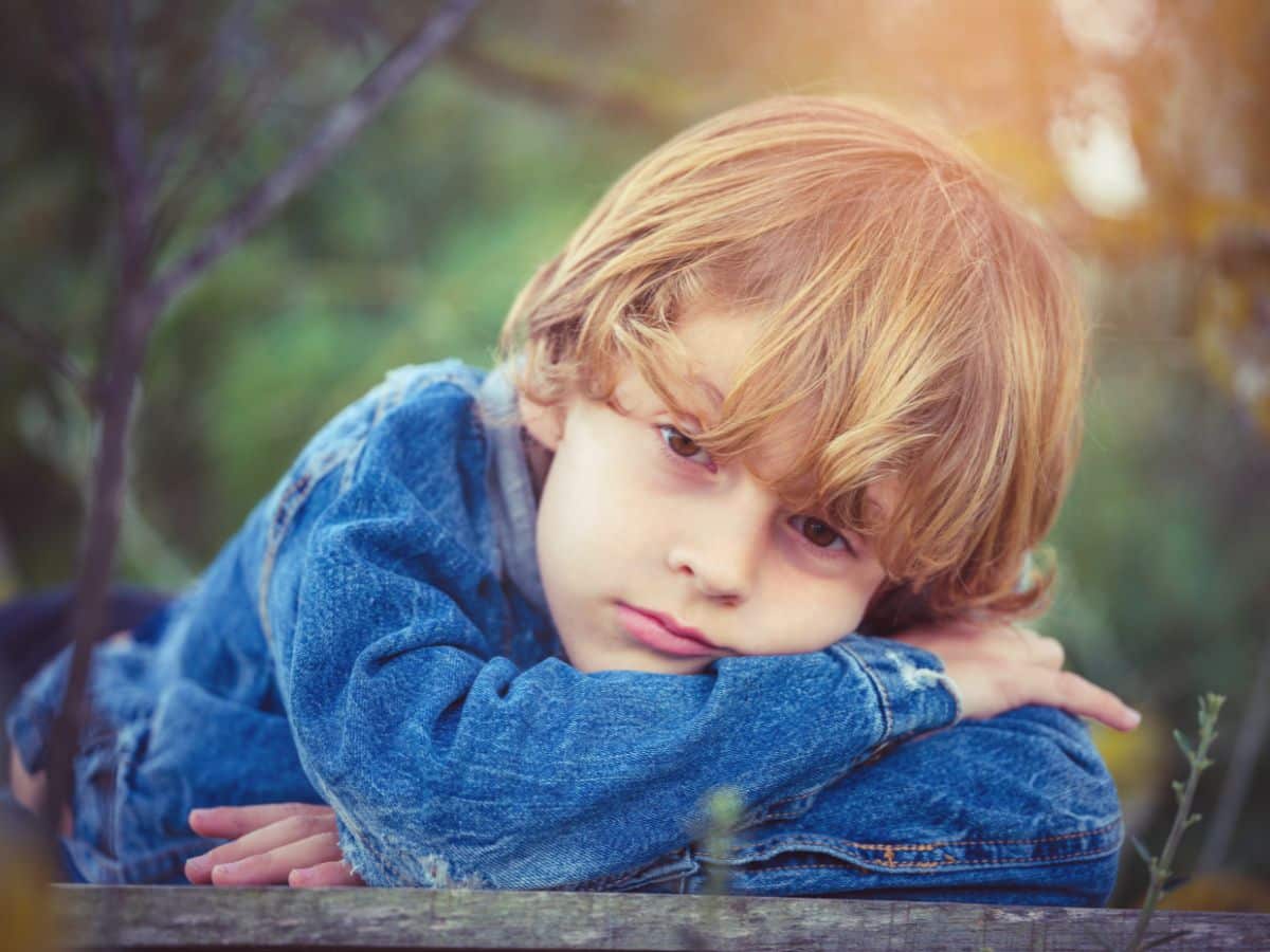 Young boy in a jean coat lying on the floor and looking bored.