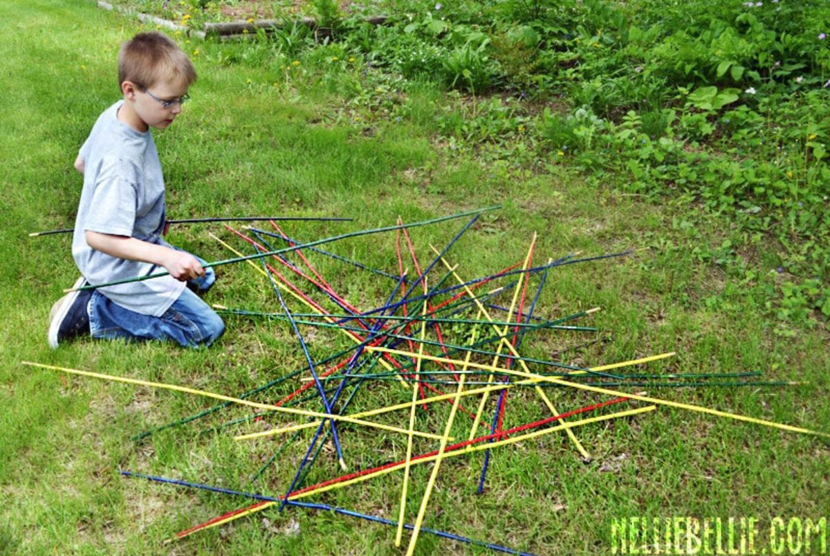 Young boy kneeling on a green grass and playing with colorful sticks.