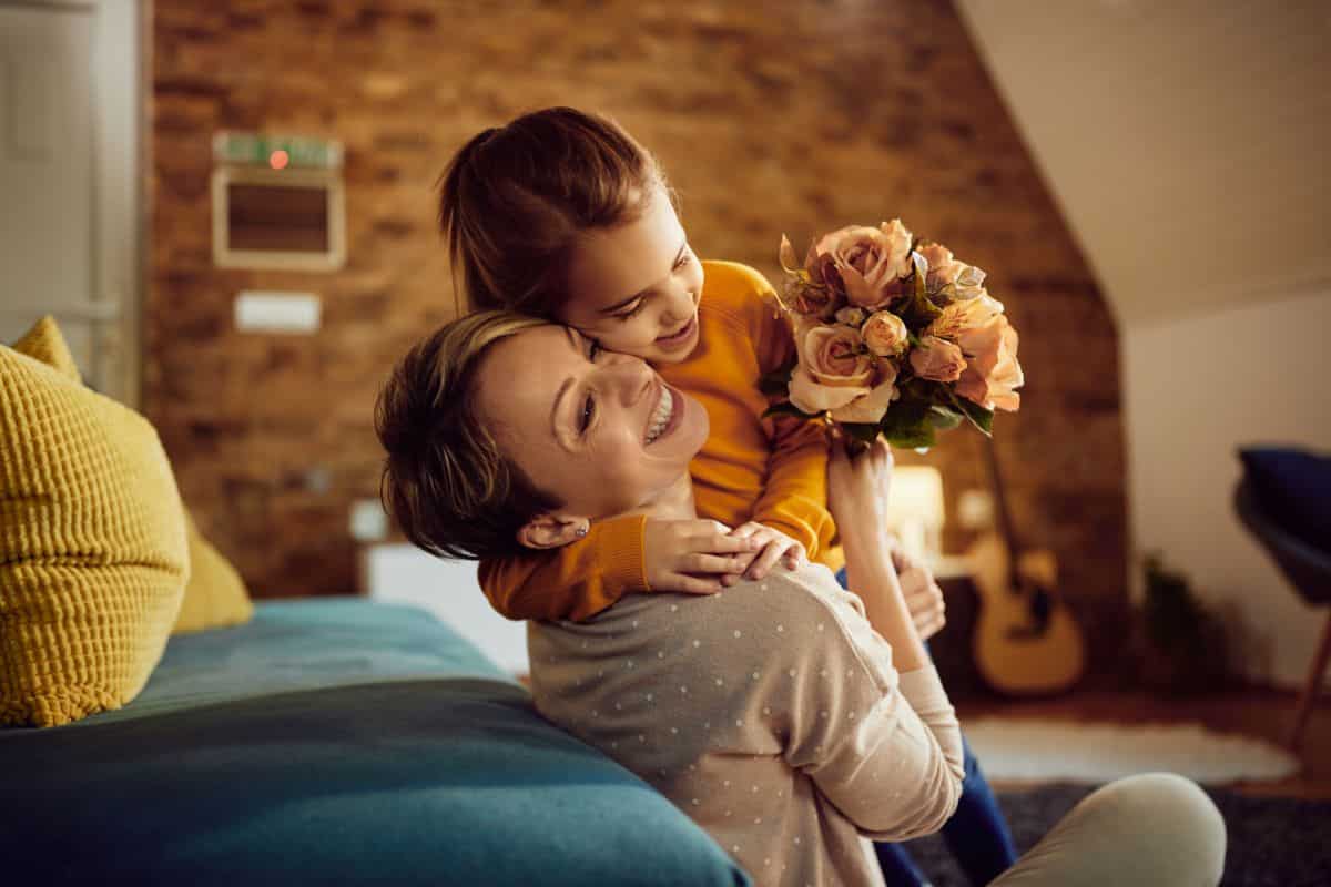 Mother hugging her young daughter while daughter holding a bouquet of flowers.