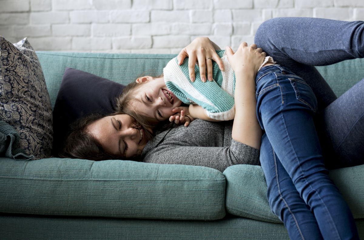 Mother hugging daughter on a green sofa.