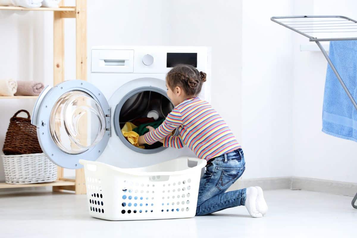 Young girl putting clothes from a washingmachine to basket.