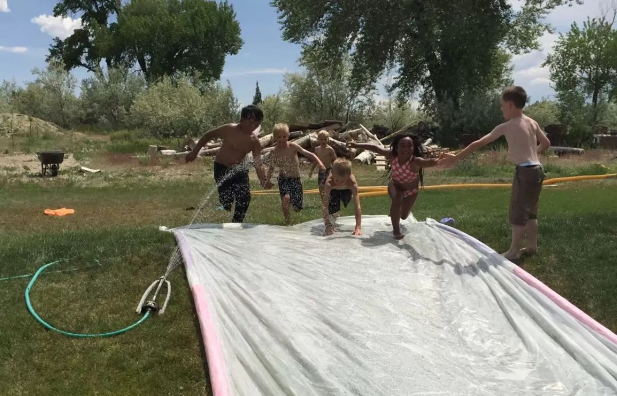 Bunch of kids playing slip-slide game outdoor.