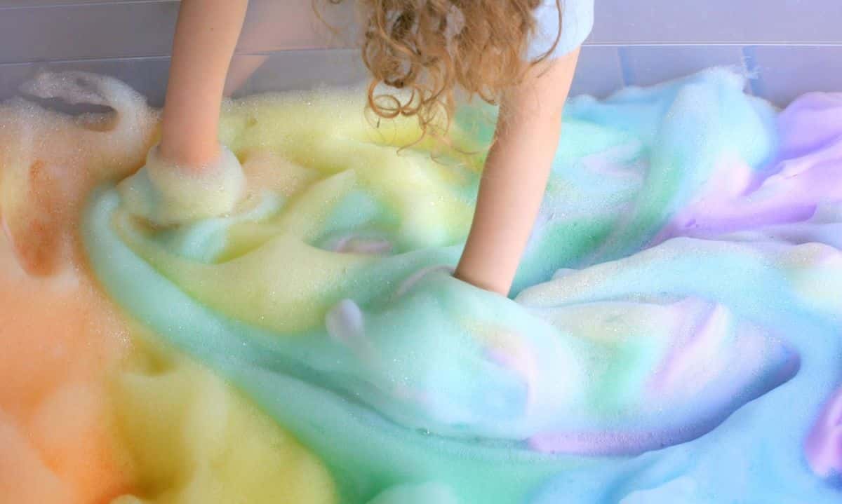 Kid is playing in a ranbow soap foam.