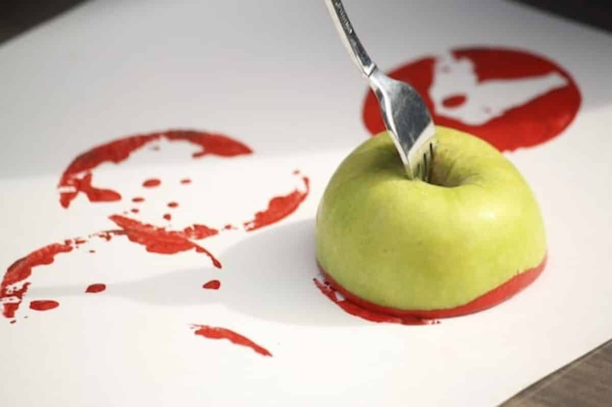 Half of apple with fork making stamps of red colour on a paper sheet.