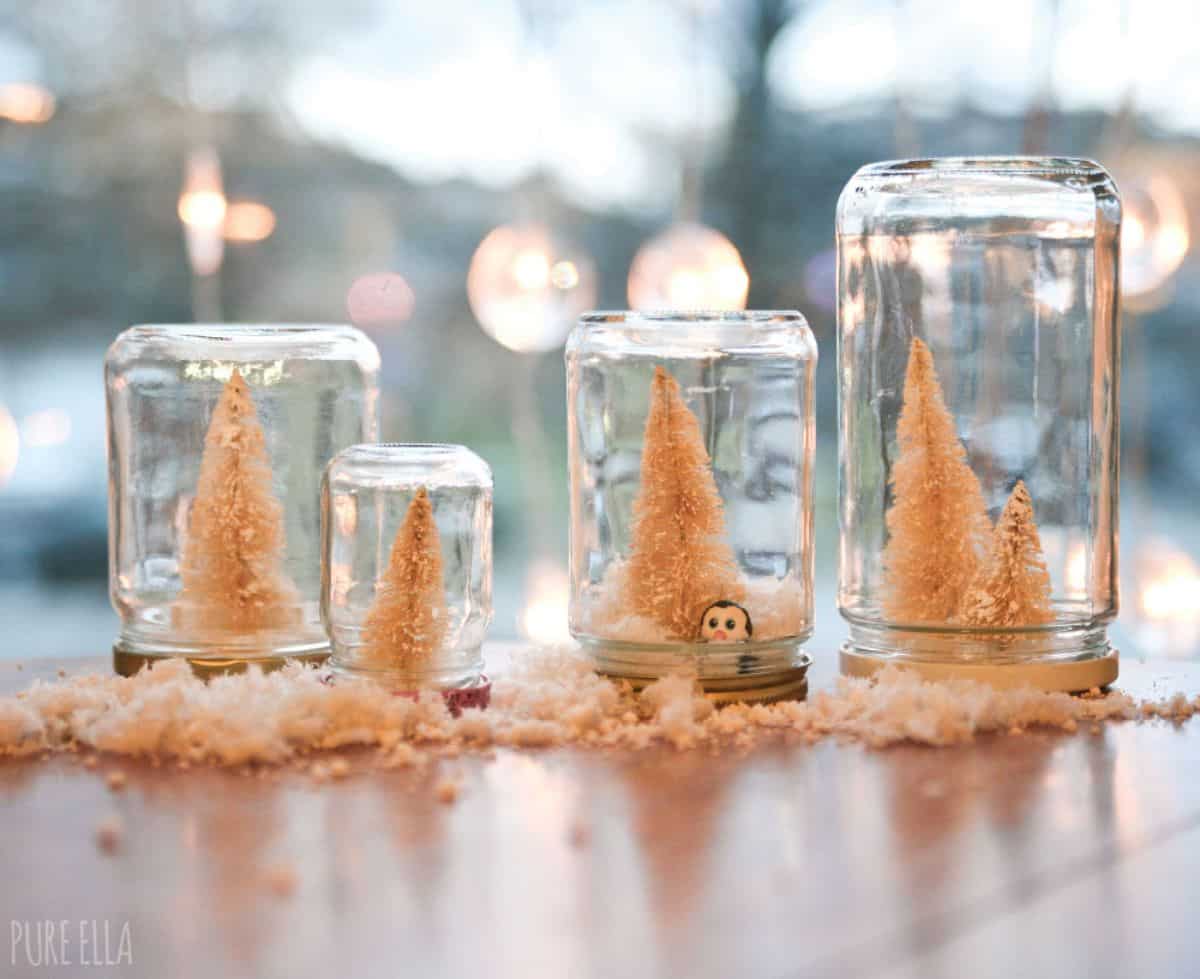 4 glass jars with christmas trees made from fake snow on a table.