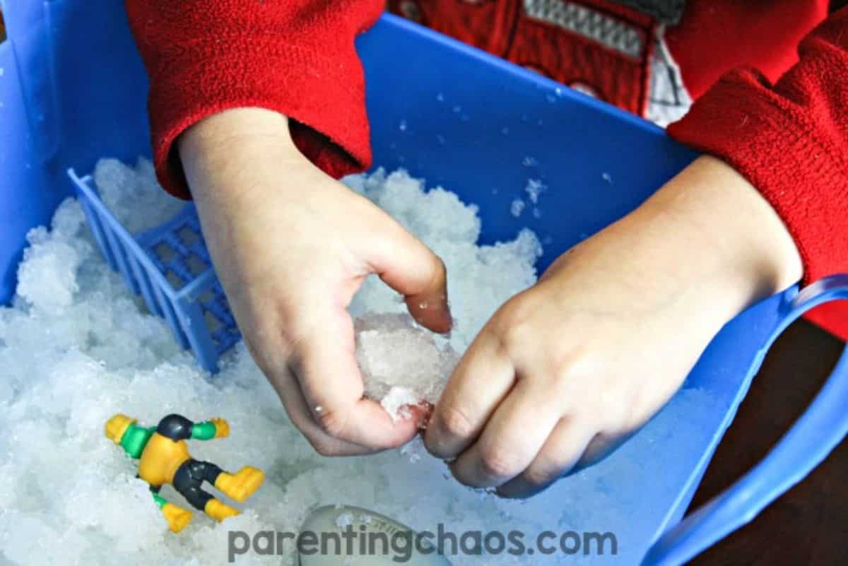 Kid in a red shirt is playing with a snow in a blue container.