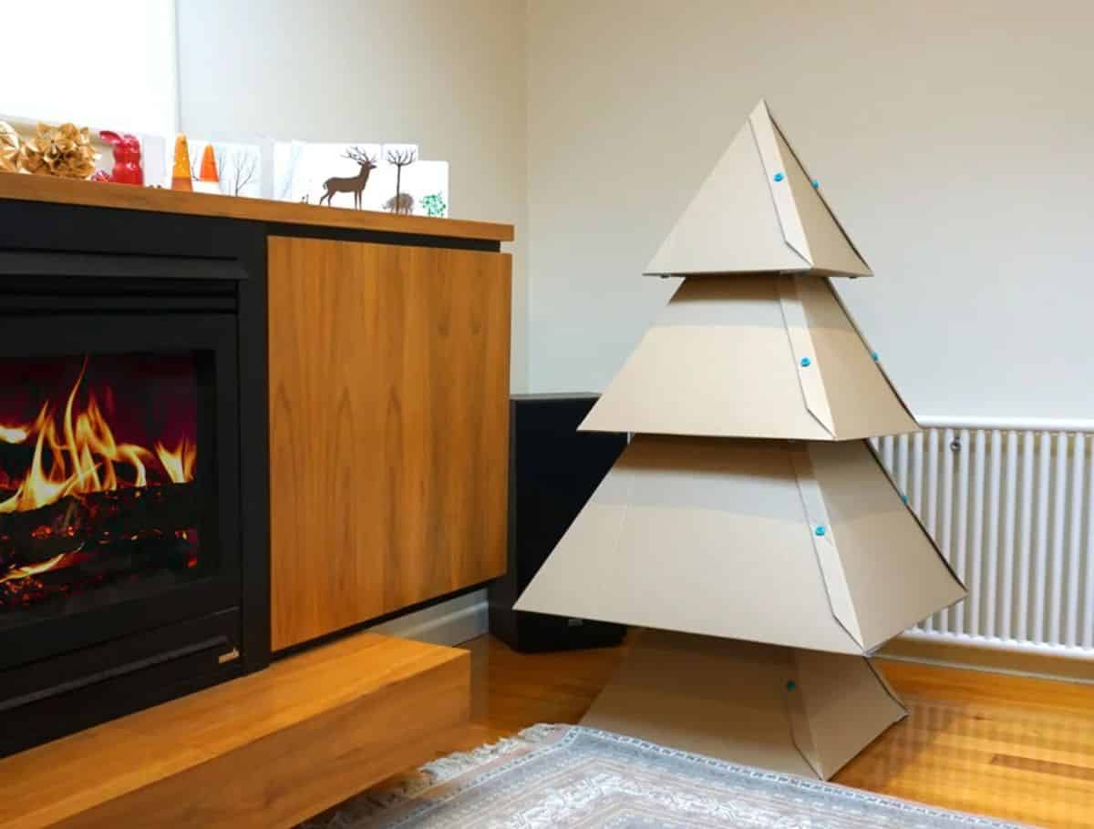 Christmas cardboard tree in a living room nex to an electric fireplace.