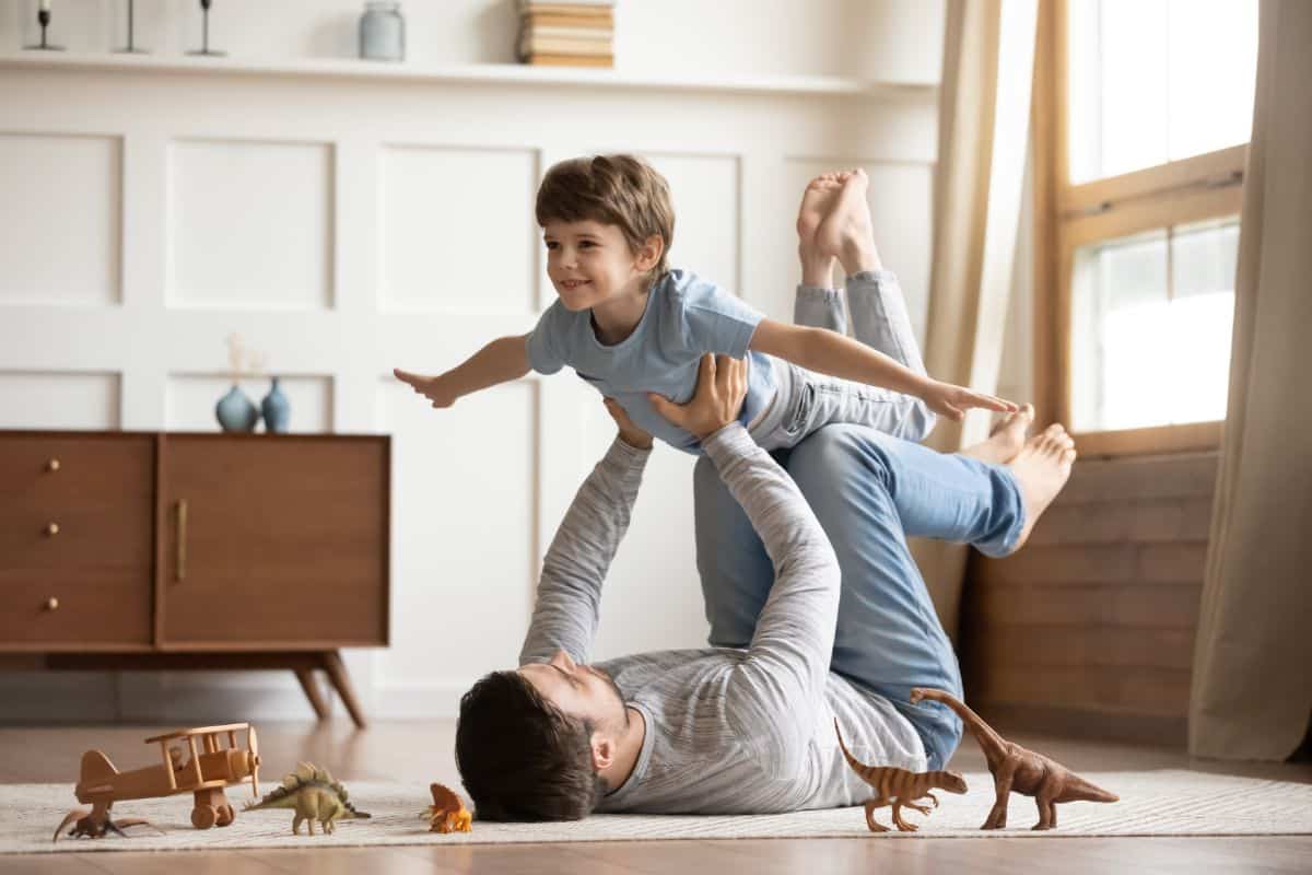 Young father holding his son  in air by hands and feet in a living room.
