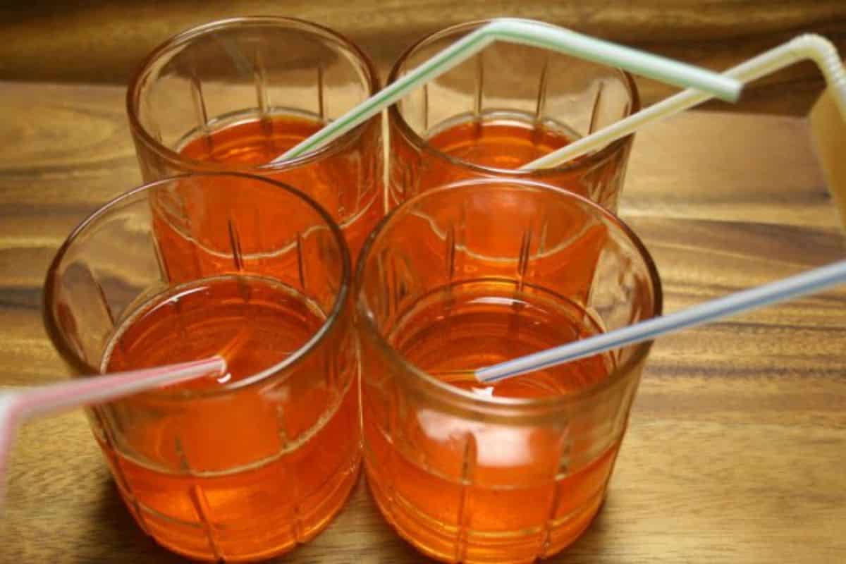 4 glass cups with a kool-aid and straw on a table.