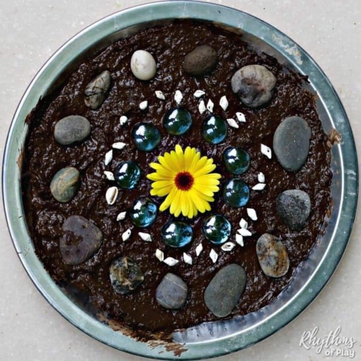 Mud pie in a mold with a yellow flower and different types of rocks.