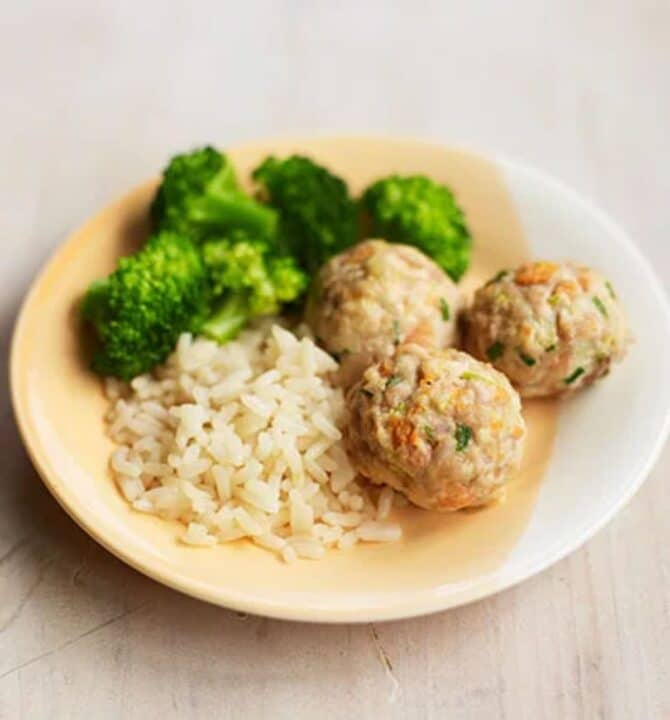 Chicken meatballs with a rice and a broccoli on a plate.