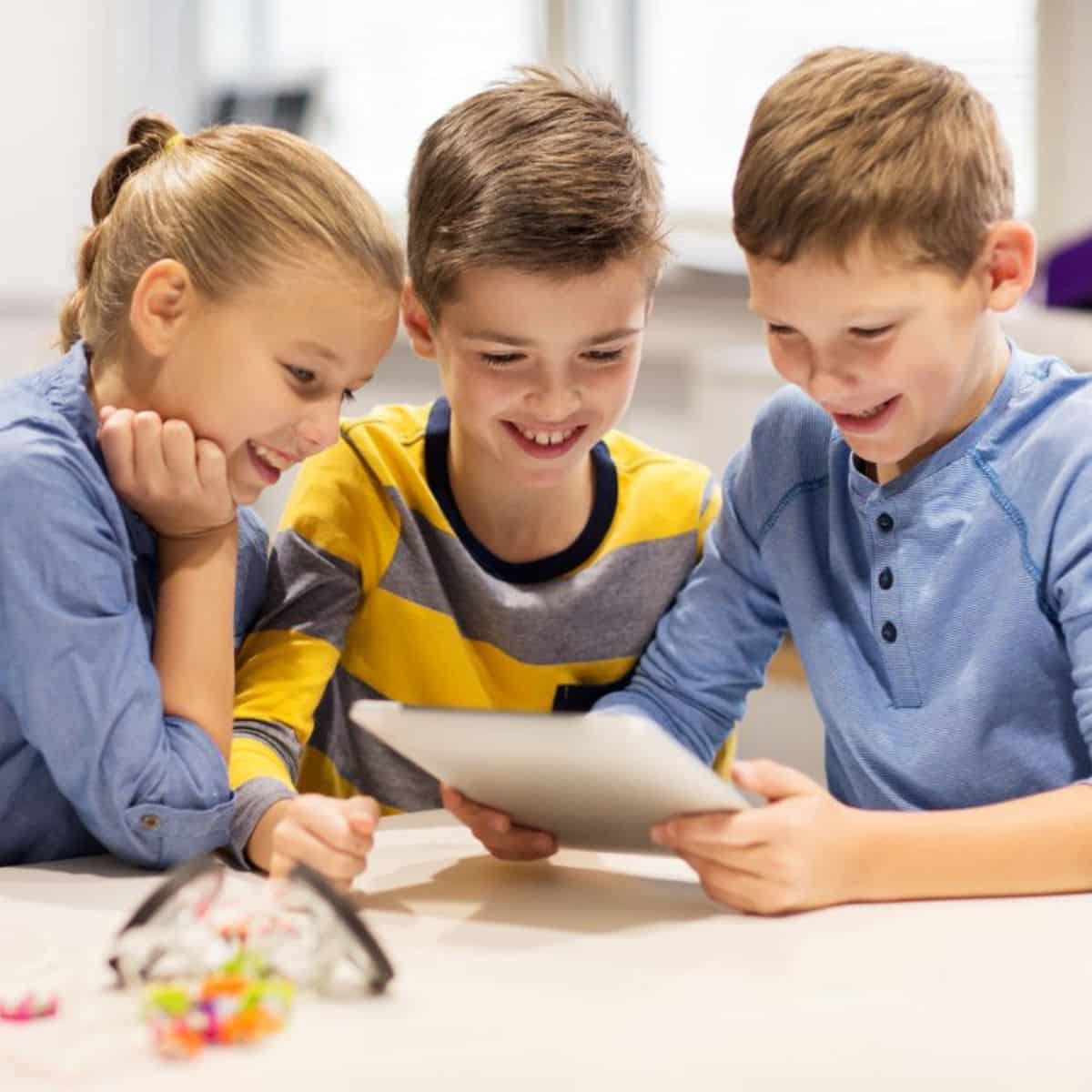 Three kids sitting at the desk and looking at a tablet.