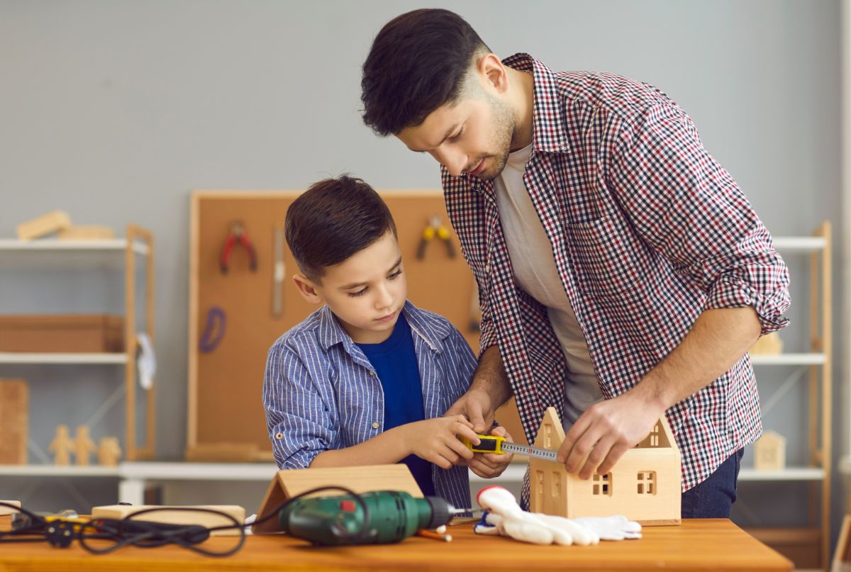 Father and son making a wooden toy house on a work bench,