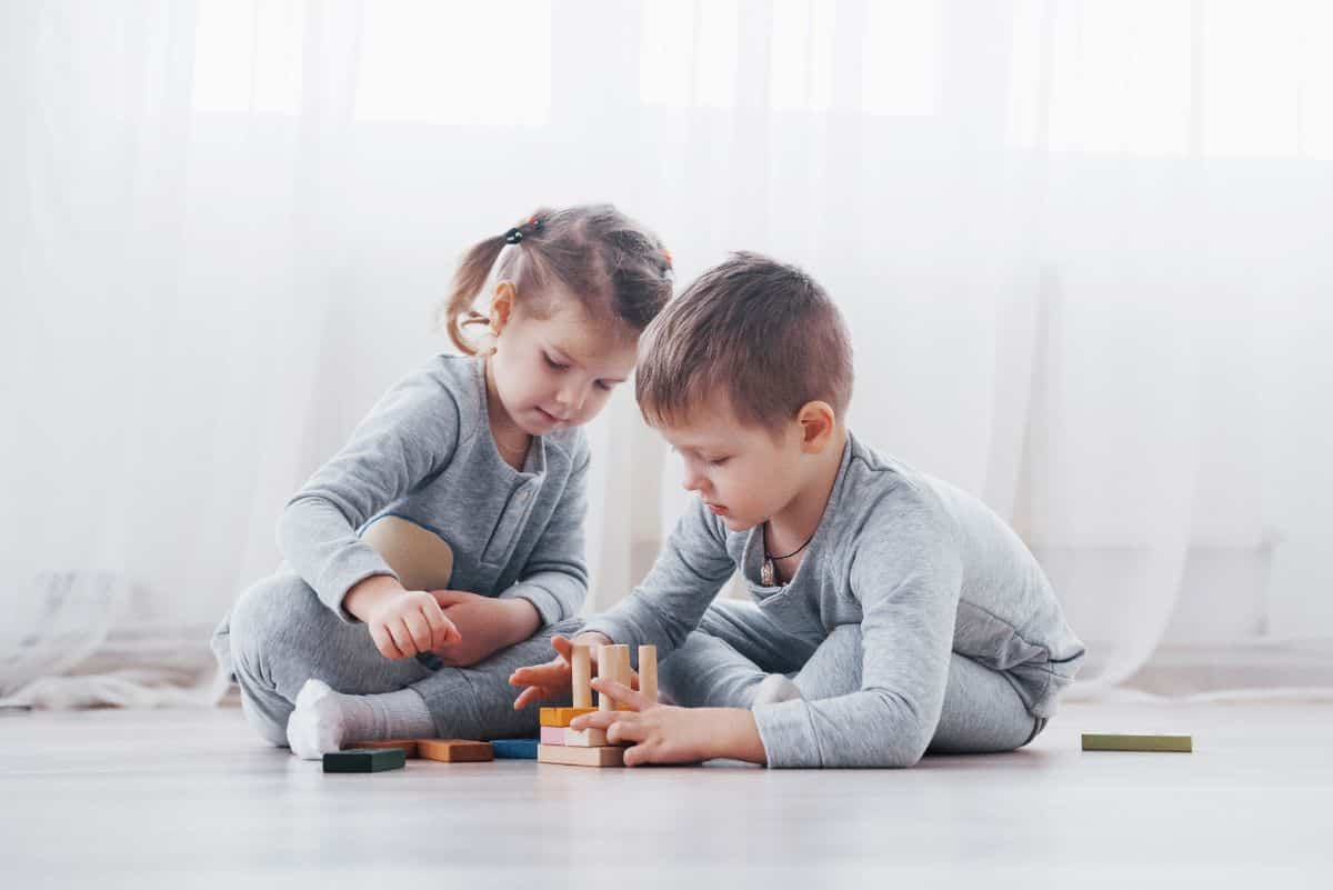 Young boy and girl are playing together on a floor.