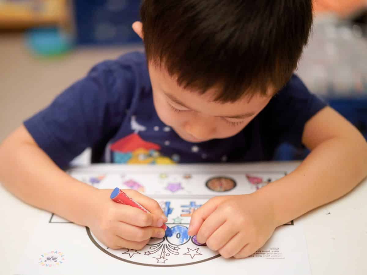 Small boy coloring with blue pencil a printed image on a sheet.