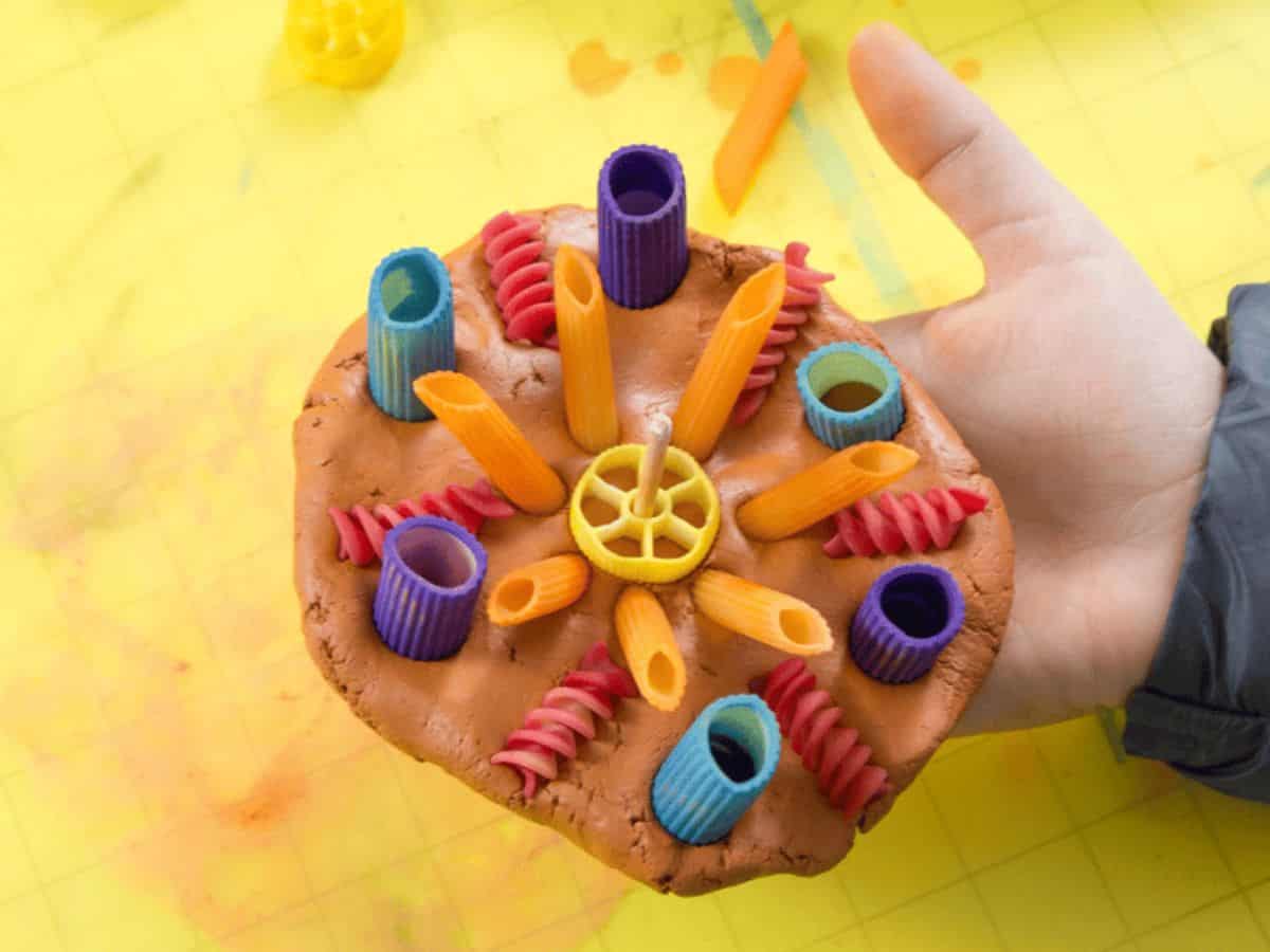 Kid's hand holding a pasta craft.