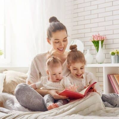 Young mother reading a book to ger two daughters on a bed.