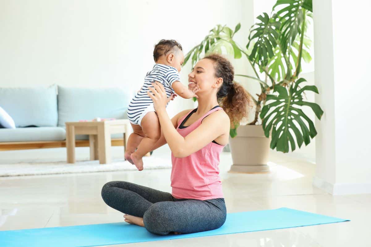 Mom sitting on a yoga pad and holding her toddler.