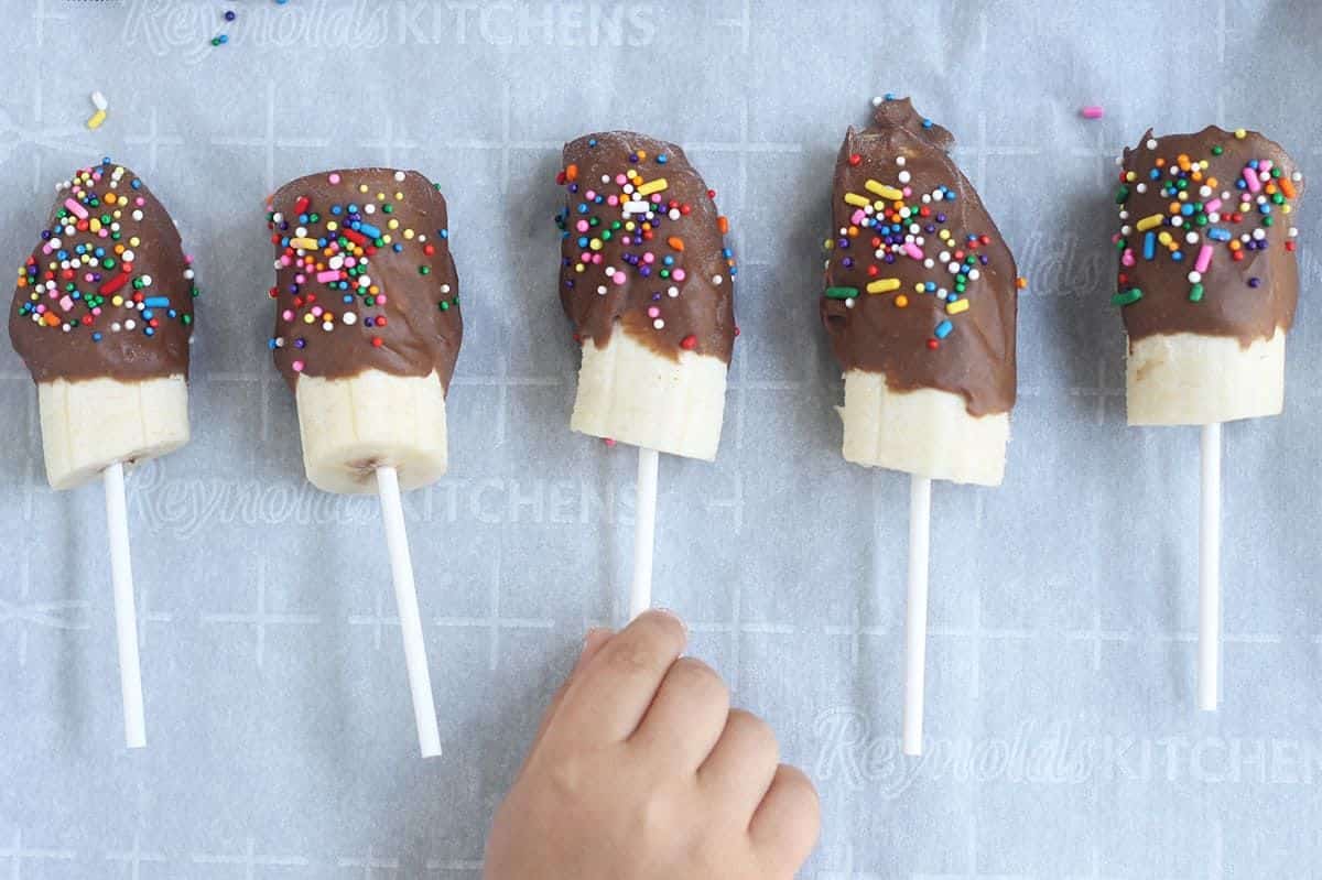Hand touching healthy banana popsicles with chocolate and avocado.