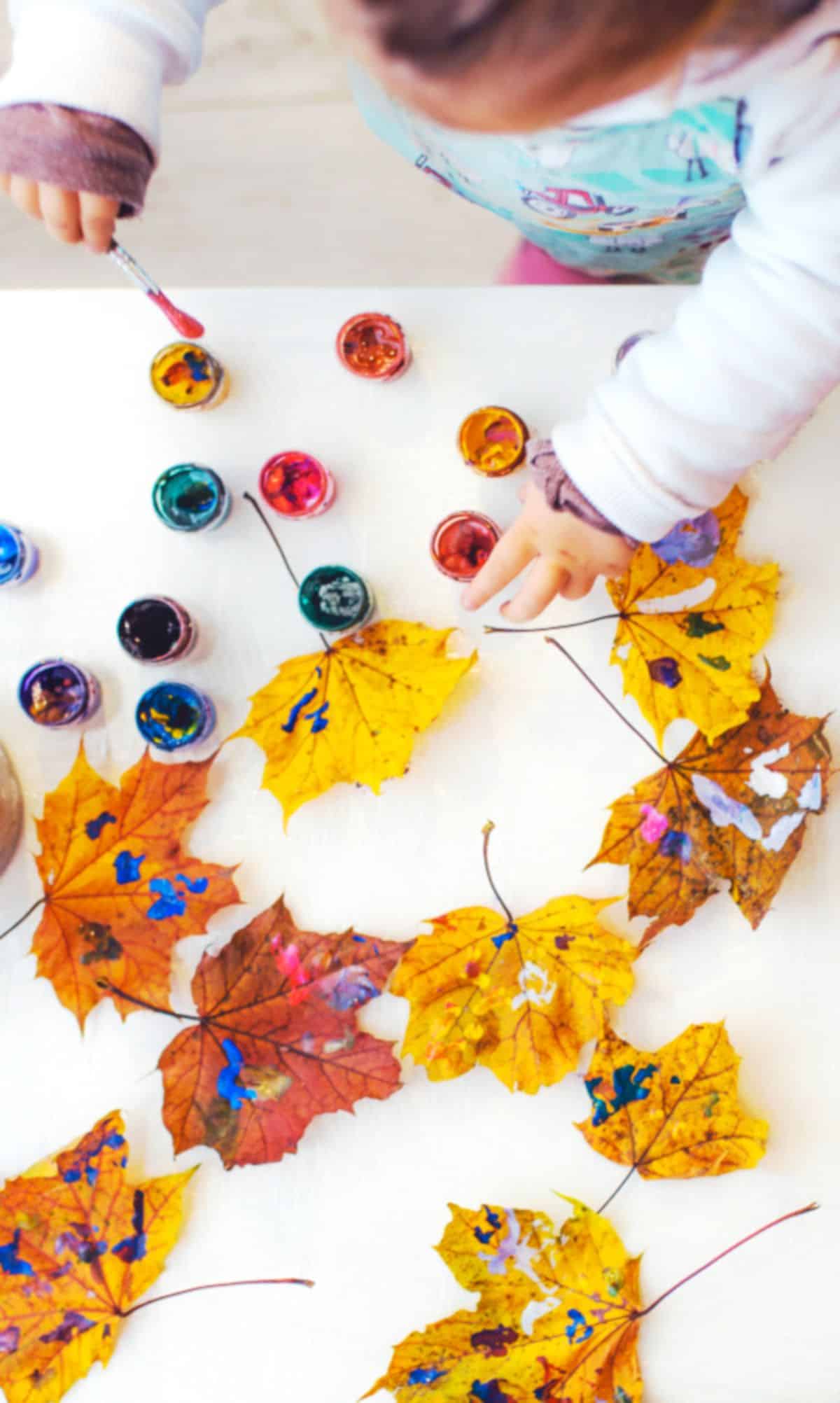 A small girl painting leaves with a brush on a table.