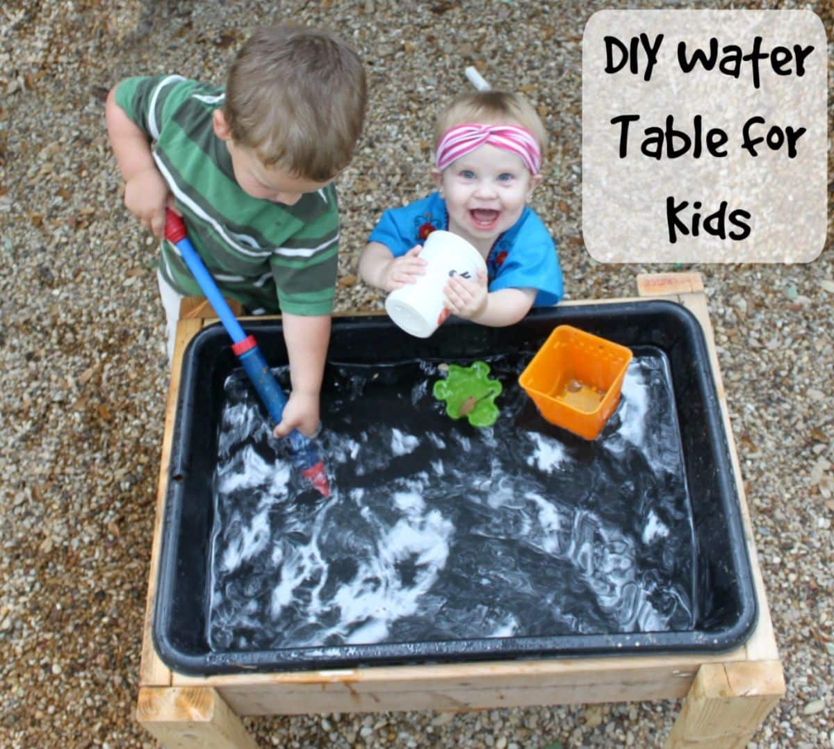 Two kids playing next to a water table outdoor.