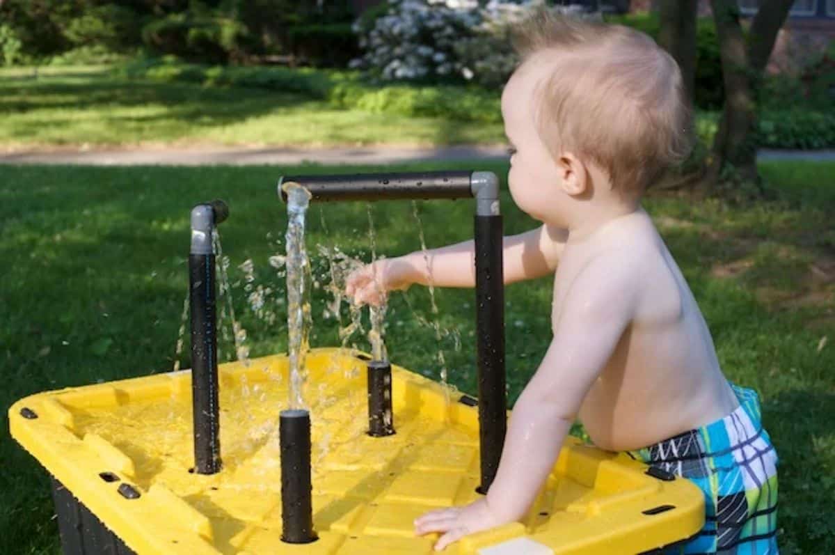 Small kid playing with water on yellow water table outdoor.