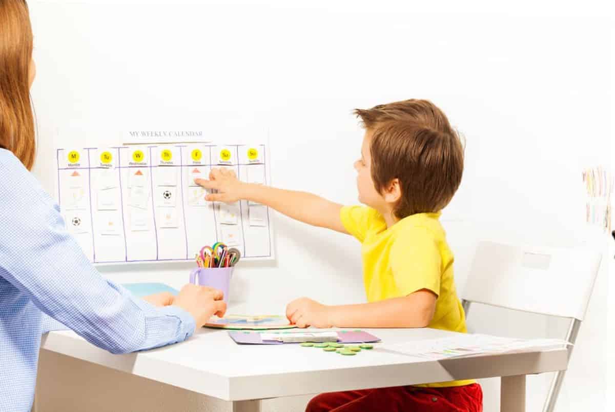 YOung boy and mother sitting at the table and boy pointing on a board.
