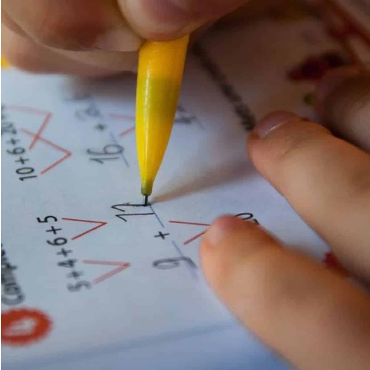 Kid with yellow pen writing number on a sheet.
