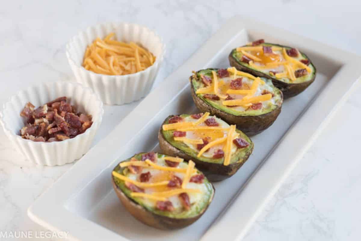 Bacon And Egg Avocado Bake on a white tray with two white bowl of ingredients.