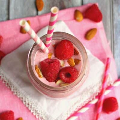 Raspberry Almond Chia Smoothie in a glass jar with two straws on a wooden table.