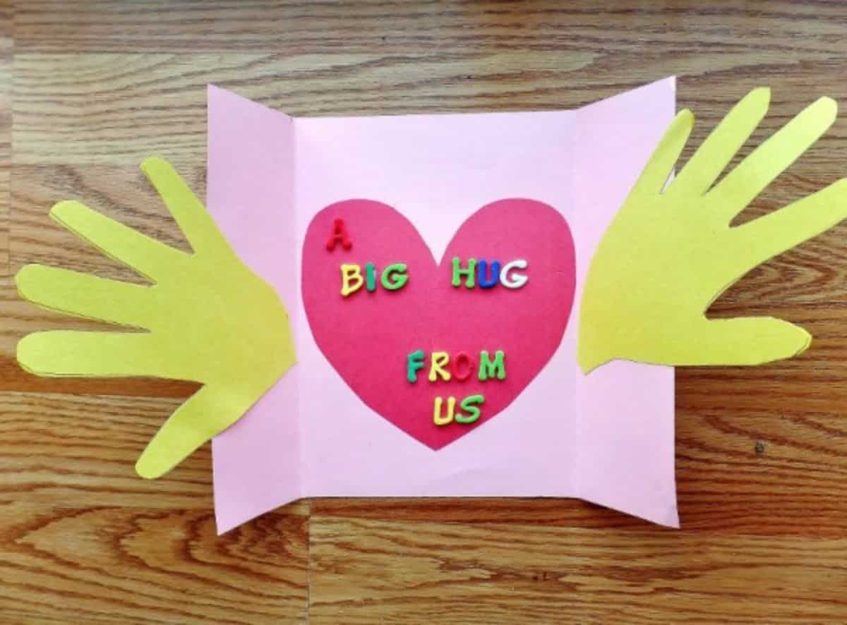 Pink paper girft with yellow paper hands, purple paper hearth with a sign - Big hug from us.