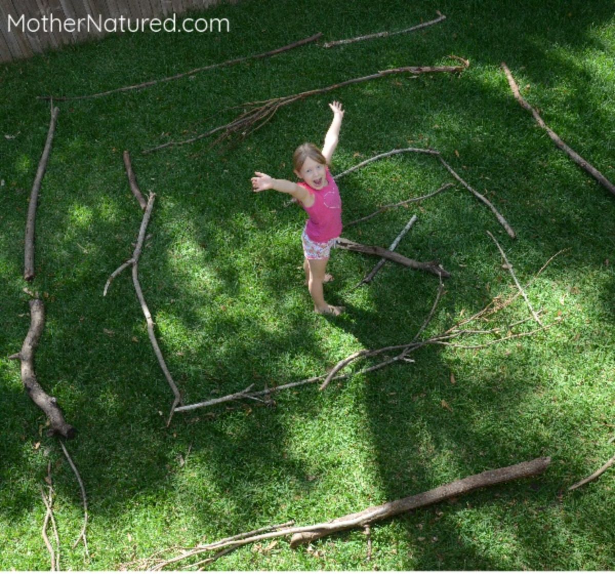 A girl stands in the middle of a patch of grass surrounded by sticks laid out in a maze