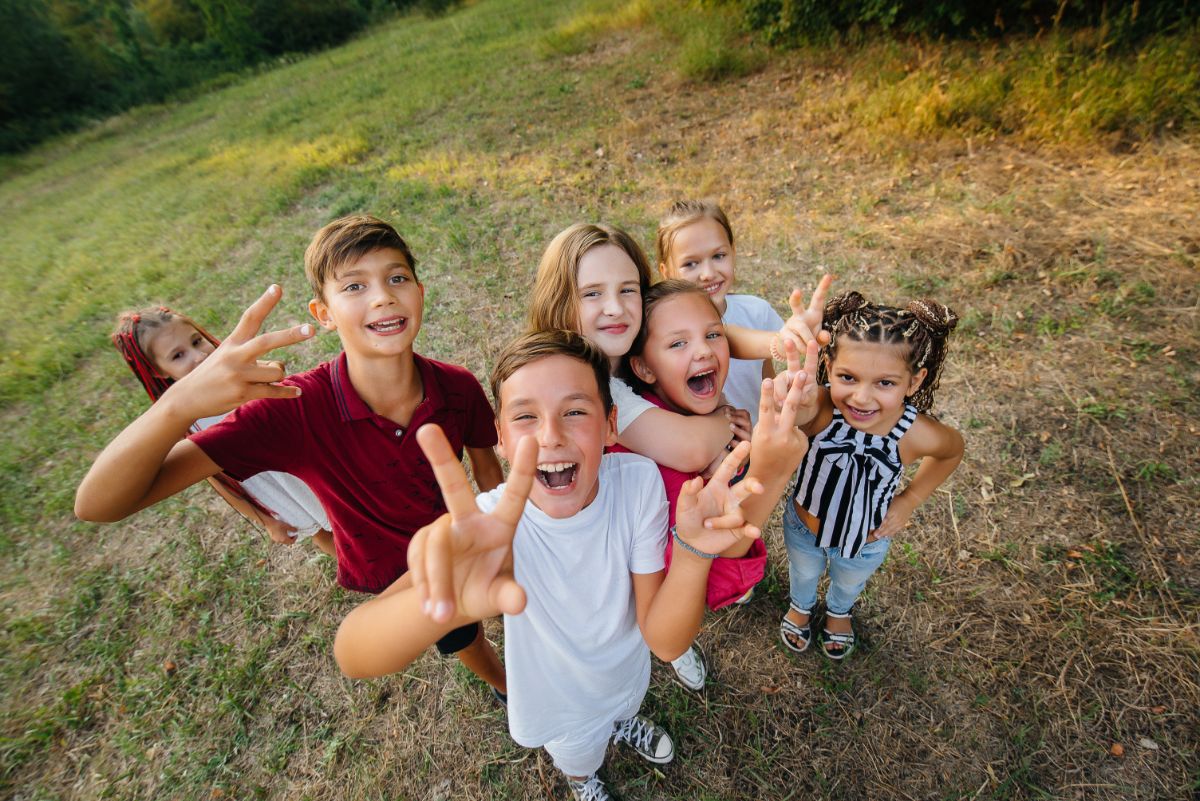 7 children stand in a group on some grass. They're looking at the camera and smiling