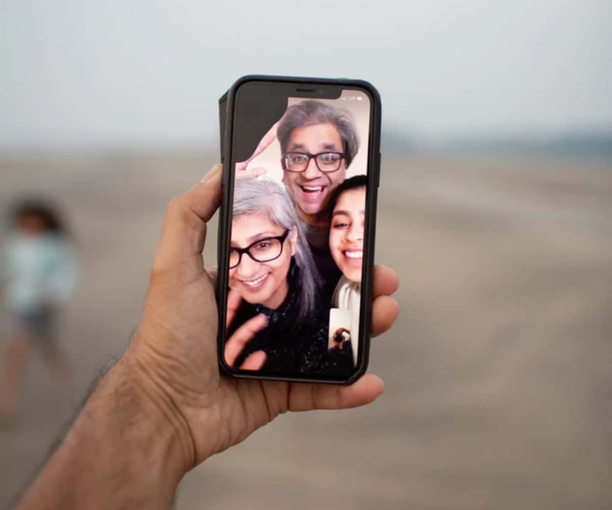 a hand holds a phone. On the phone are 3 faces in a facetime call