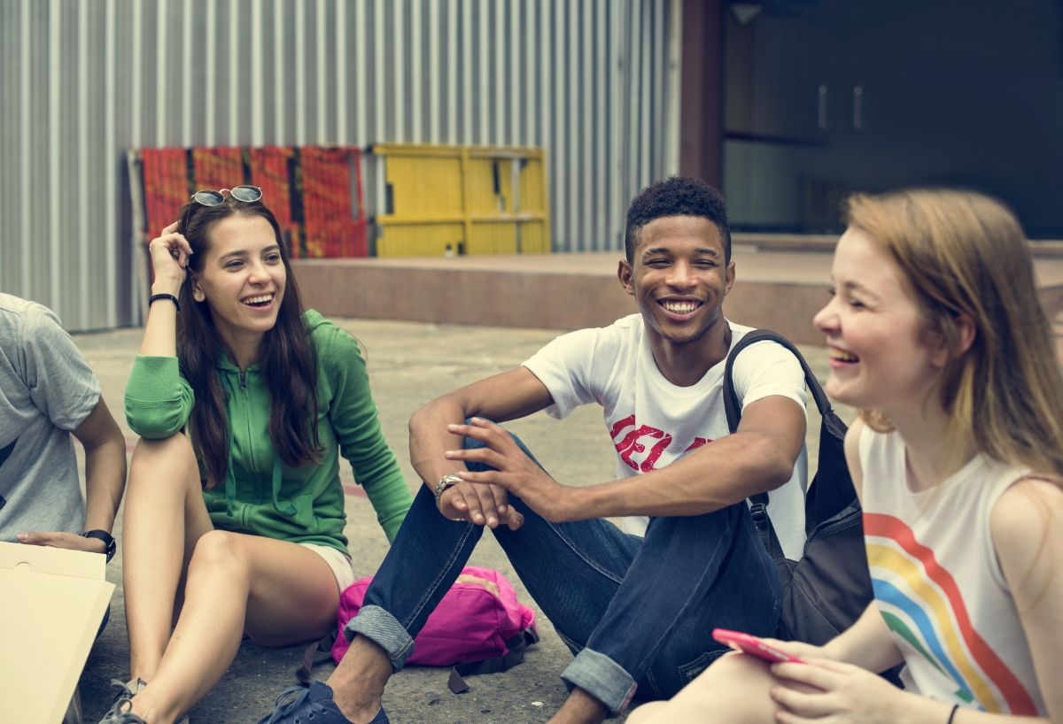 4 teenagers sit on the floor of a yard, smiling at each other