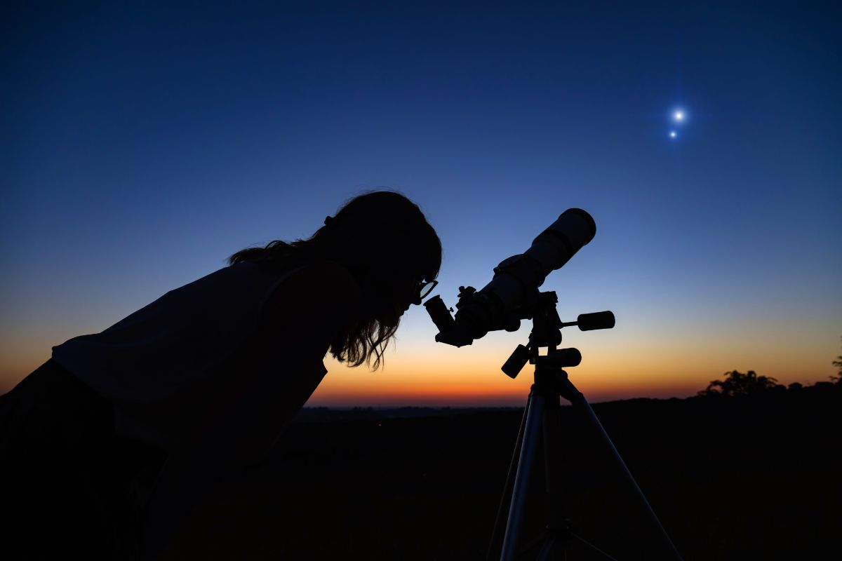a sillhouette of a woman looking through a teelscope at the night sky