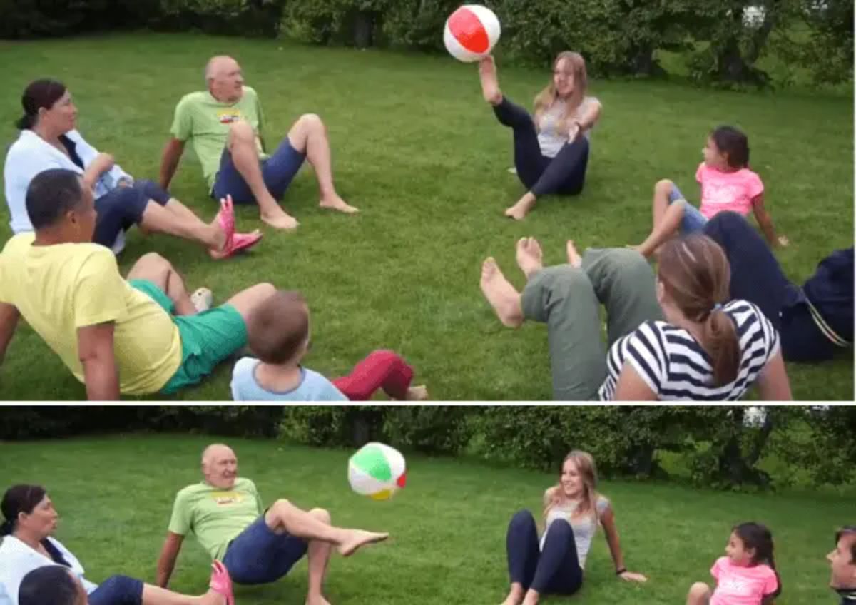 A group of people sit in a circle and kick a beach ball between them
