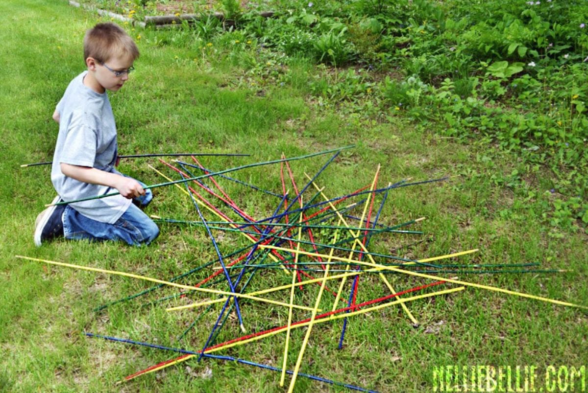 a child kneels on some grass with a group of yard pick up sticks in front of him