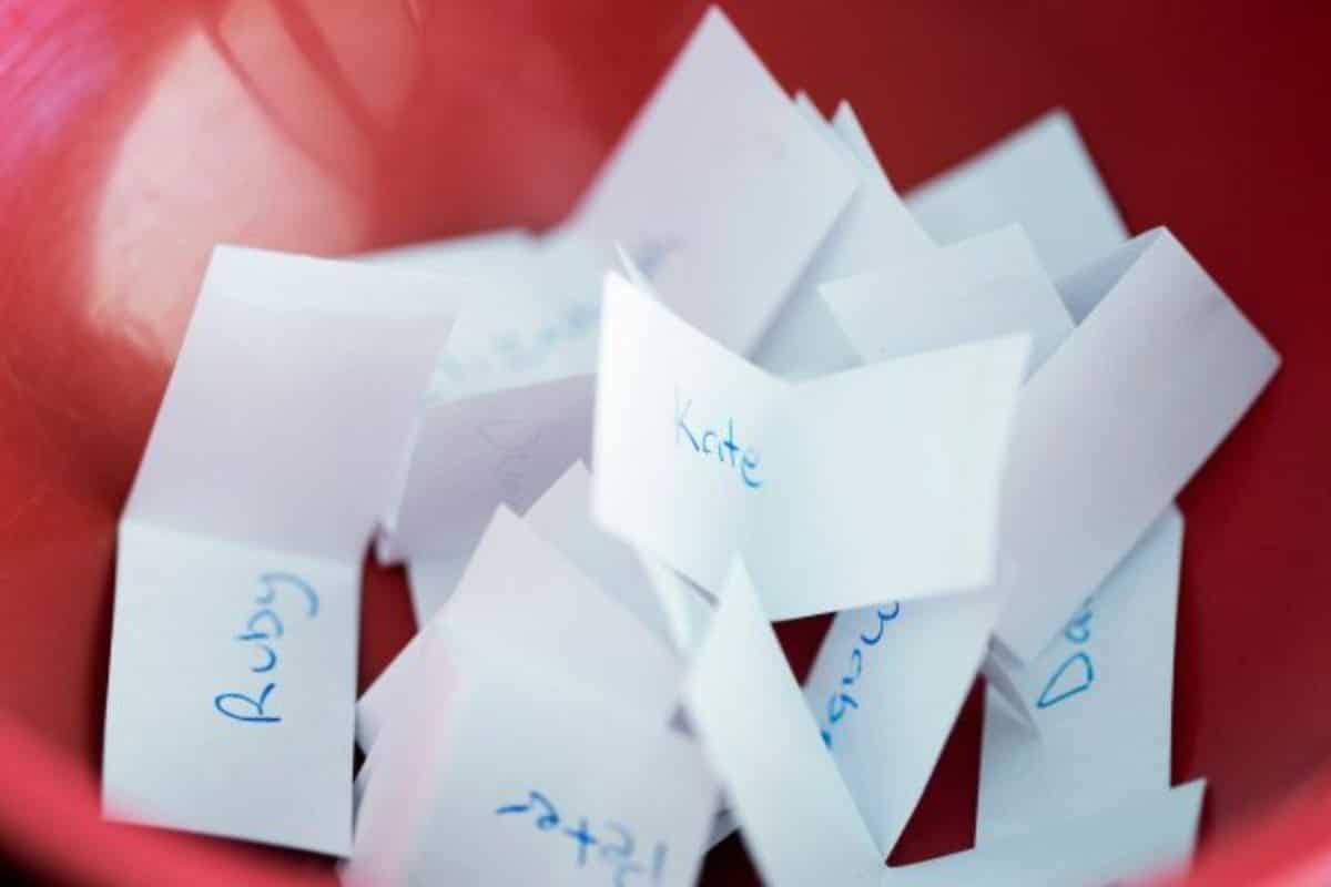 a close up of a red bowl filld with white slips of paper on which are written names