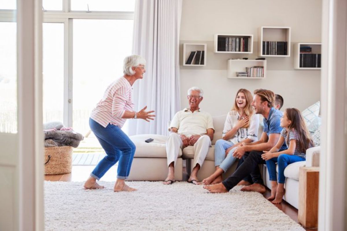 A family sits on a cream sofa in a light and airy living room. Grandma is standing in front of the sofa gesticulating