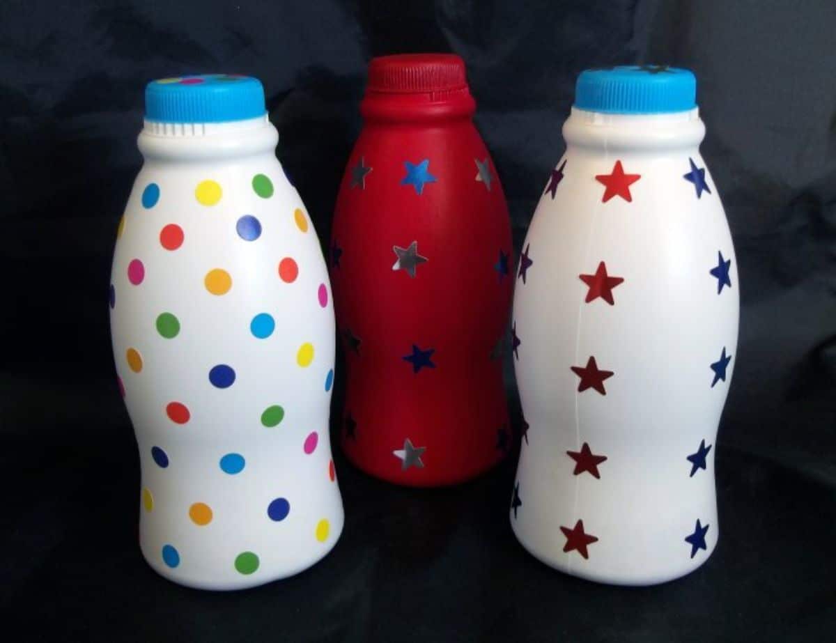 2 white and one red painted bottles with spots and stars on them against a lack bacnground