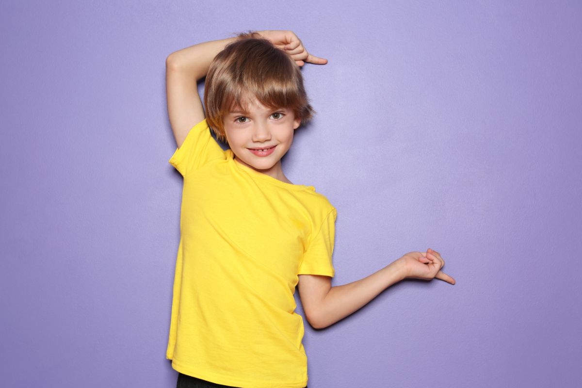 on a purple background is a young boy with a yellow shirt pointing to his left