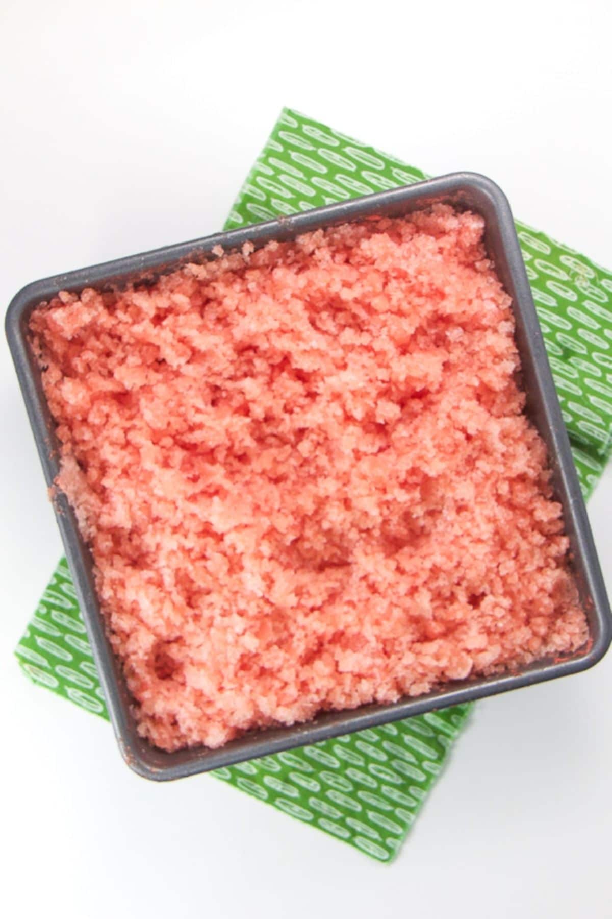 on a green cloth is a square bowl full of watermelon slush